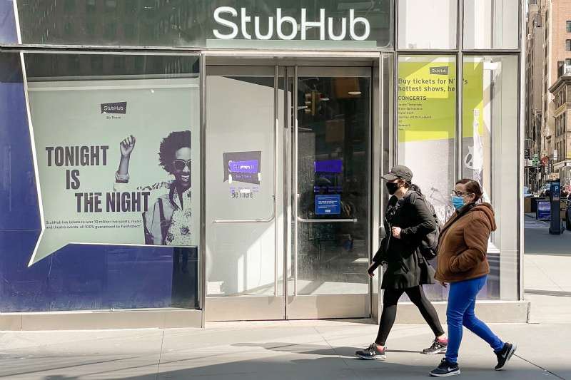 People wear face masks as they walk by a StubHub location in New York City