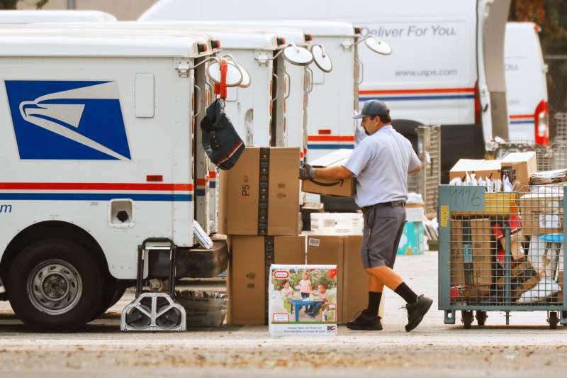 Mail carrier loading packages onto a United States Postal Service truck