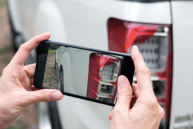 Close up of hand taking a photograph of a shattered car light with a smartphone