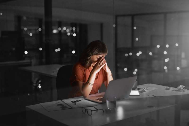 Young businesswoman looking stressed out while working in an office late at night on her laptop