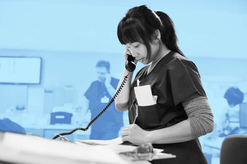 Photo of a nurse checking notes while talking on phone
