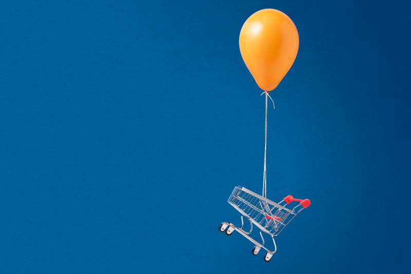A shopping cart is elevated by a helium balloon up in the sky, symbolizing inflation.