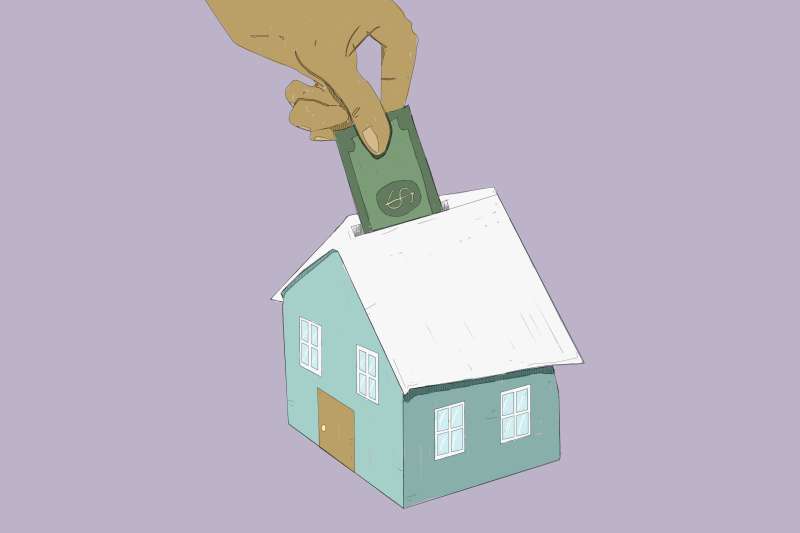 Hand Placing Dollar Bill Into House Shaped Piggy Bank