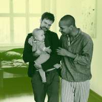 Two fathers holding their baby son in the nursery.