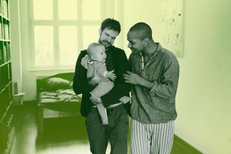 Two fathers holding their baby son in the nursery.