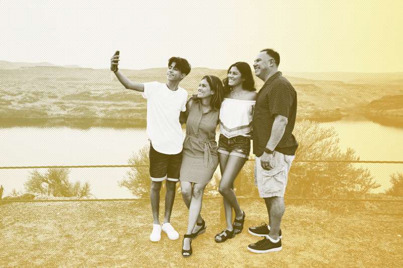 A family of four taking a selfie outdoors on a sunny day.