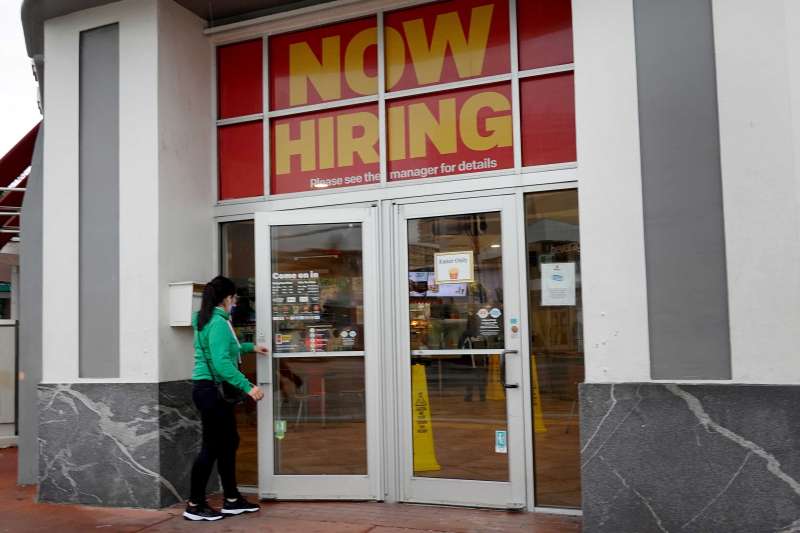 Woman Walking Into A Store That Has A Large Now Hiring Sign