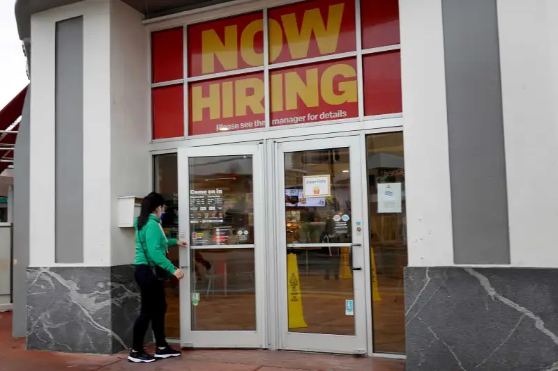 Woman Walking Into A Store That Has A Large Now Hiring Sign