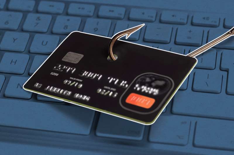 Photo of a credit card being caught in a fishing hook on top of a computer keyboard