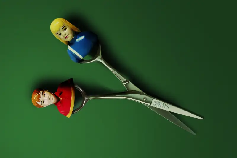 Photo-Illustration of a pair of scissors with the IRS logo, where one side of has a toy figure of a girl and the other a toy figure of a boy