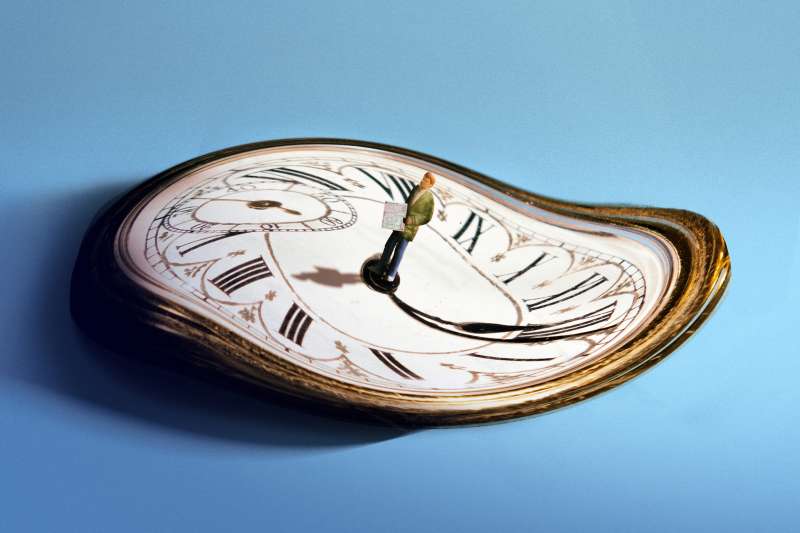 Photo-Illustration of a man standing with a 1040 Tax Form on top of a distorted clock