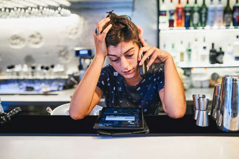 Young, frustrated woman working at a bar deals with customers