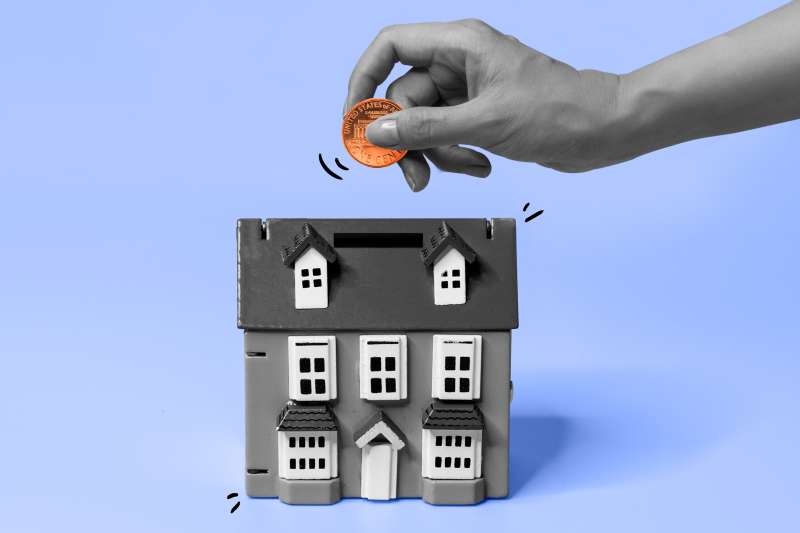 A hand inserting a penny into a house shaped coin bank.