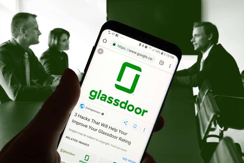 collage of a hand holding a smartphone with the Glassdoor logo with an image of two people interviewing a potential candidate in the background