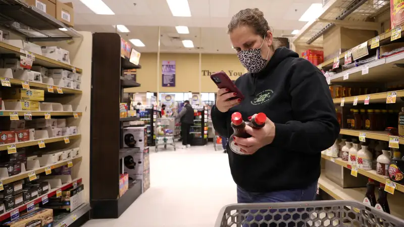 Woman compares prices of maple syrup at a grocery store before buying them