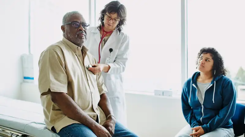 Female doctor using stethoscope to listen to senior male patients breathing during medical exam