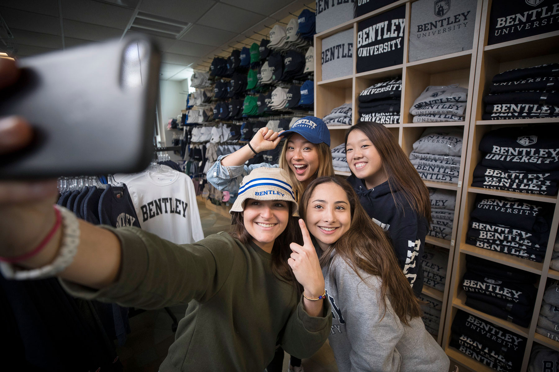 A group of girls take a selfie while wearing Bentley University merchandise