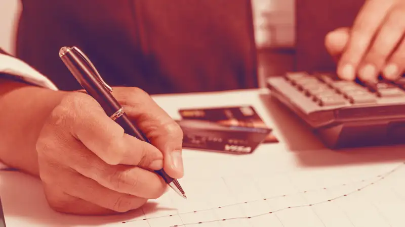 Close up photo of a person making anotations, using a calculator and verifying their credit cards