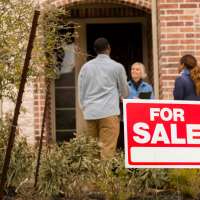 Couple Talking With Realtor In Home Entrance In front Of For Sale Sign