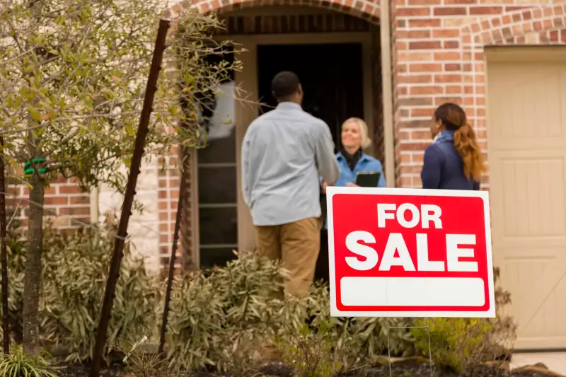 Couple Talking With Realtor In Home Entrance In front Of For Sale Sign