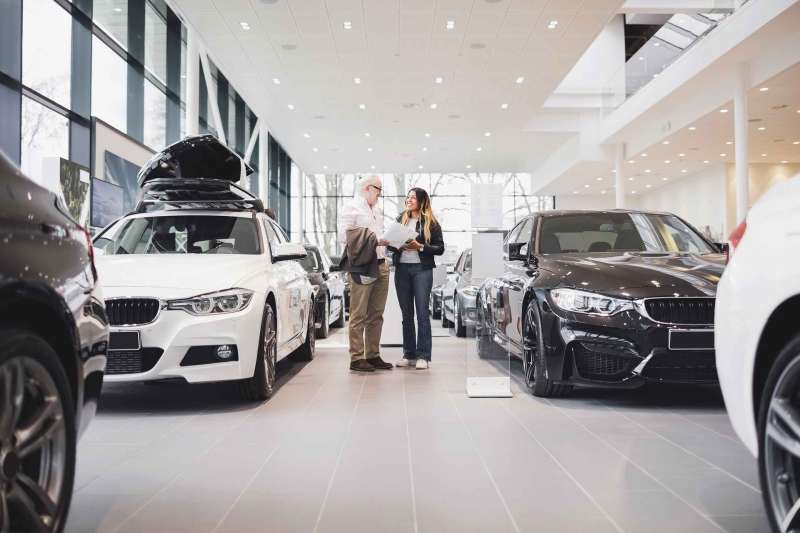Man and woman with paper standing amidst cars at showroom