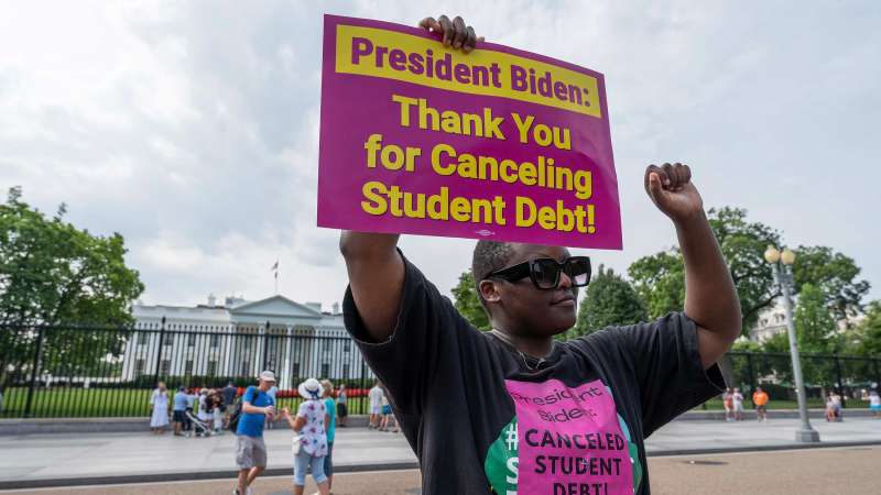 Woman with a sign in front of the White House that reads  President Biden: Thank you for canceling student debt!