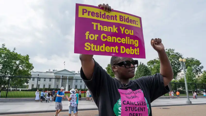 Woman with a sign in front of the White House that reads President Biden: Thank you for canceling student debt!