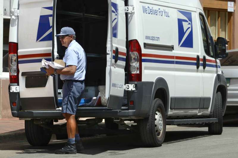 Mailman Holding Packages In Front Of Mail Van
