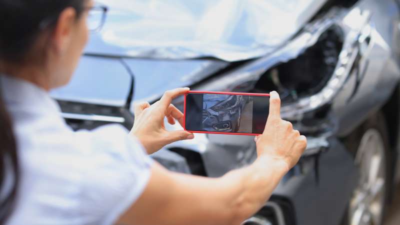 Woman taking a picture by smartphone of car damage after road accident