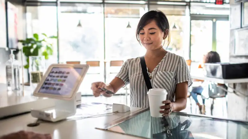 Young woman using credit card reader at coffee shop counter