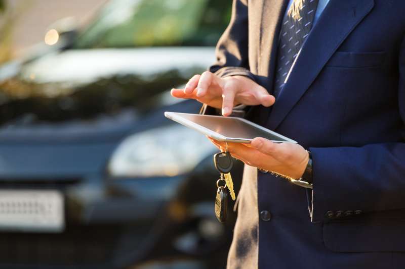 Closeup of a man holding car keys and using a digital tablet
