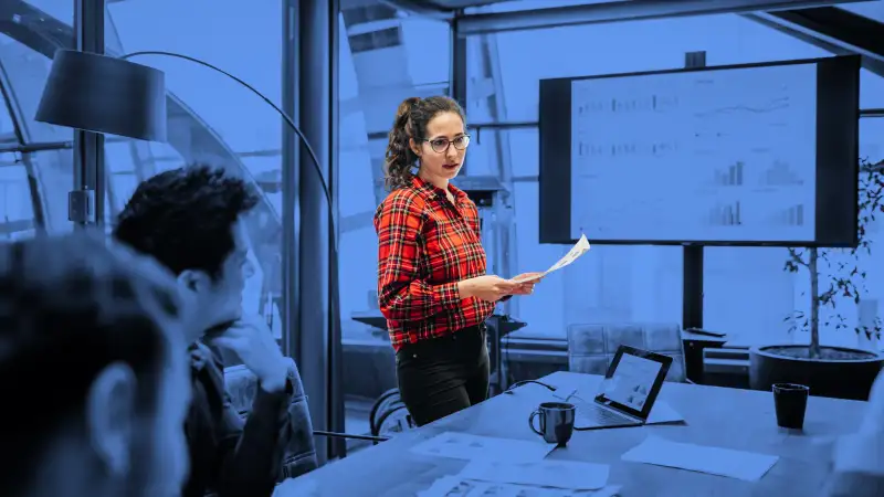 A young woman looking over some charts and data with her colleagues during a management meeting in a contemporary office space.