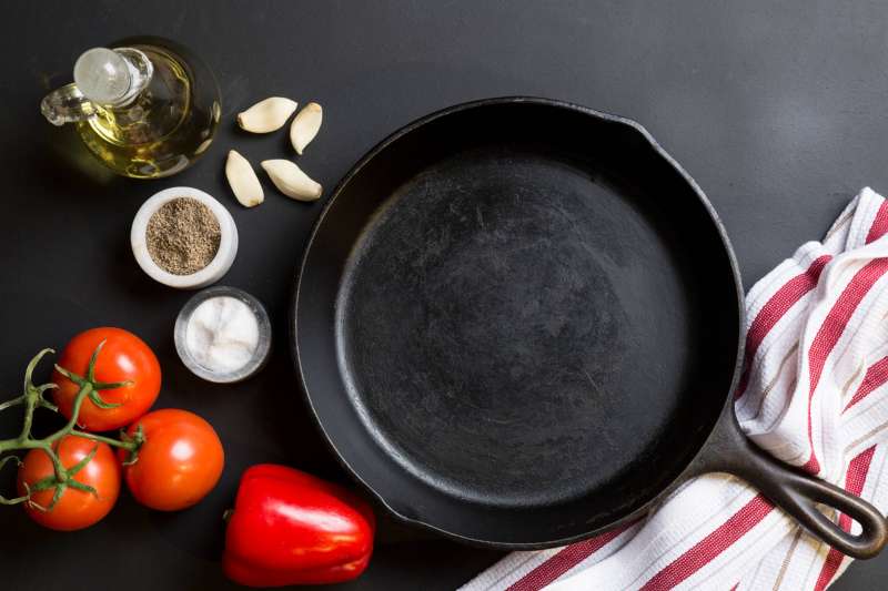 Pre-seasoned skillet on counter next to oils, spices, and produce.