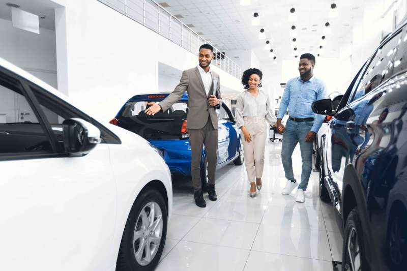 Car Selling Business. Manager Showing Luxury Automobile To Spouses In Automobile Dealership Center.