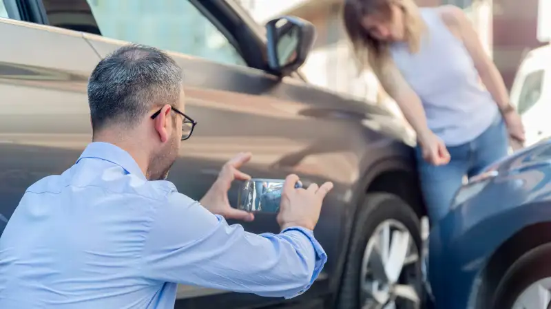 Man taking a picture with his phone of his car damage after an accident