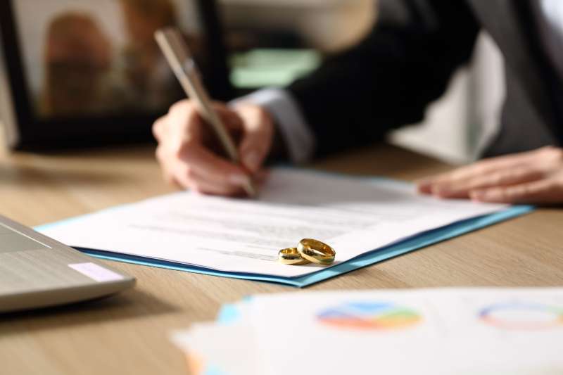 Close-up of a person signing divorce papers with the two wedding rings on the side