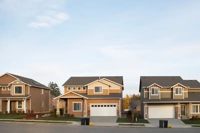 Row of houses with garbage and recycling bins on roadside.