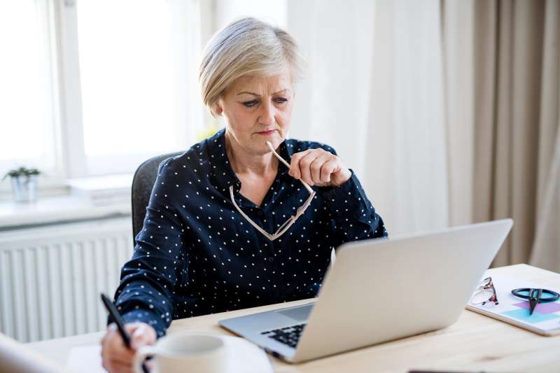 A portrait of active senior woman with laptop working in home office.