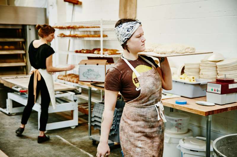 Female baker carrying dough on pastry board through bakery