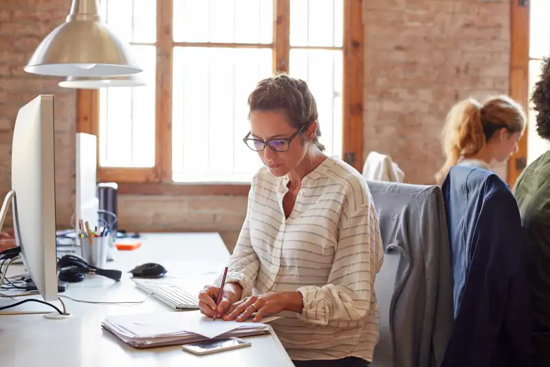 Woman writing notes at desk in office