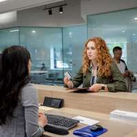 Young female client with debit card talking with bank teller in bank