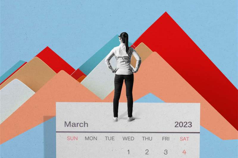 Person standing on top of and oversized march 2023 calendar overlooking stock market graphics in the shape of mountains