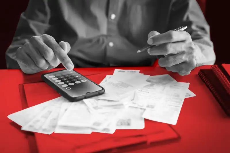 Close-up of a person using the calculator on their smartphone while looking over receipts