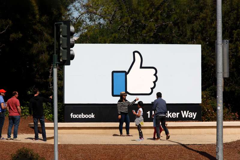 People posing in front of Facebook sign