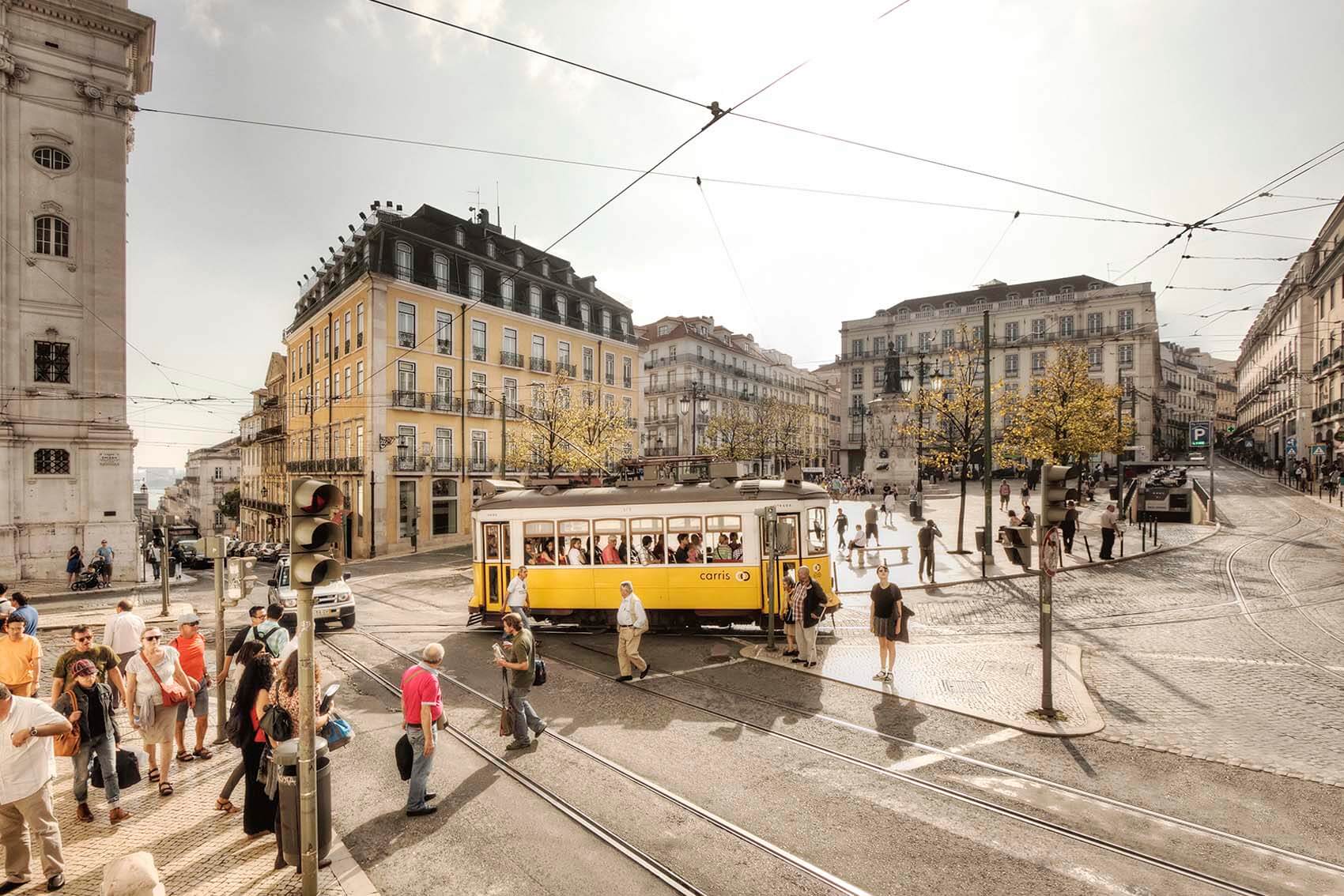 People crossing the street with a yellow tram train in the background in Lisbon, Portugal