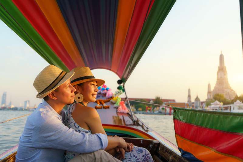 Attractive mixed race romantic couple sightseeing Wat arun in Chao Phraya River with longtail boat tour along the river in Bangkok, Thailand