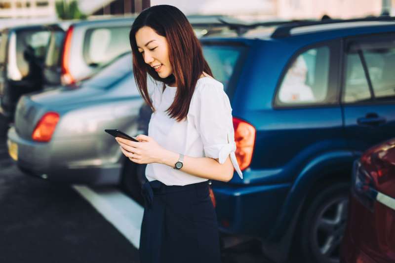 Young businesswoman reading emails on smartphone next to car