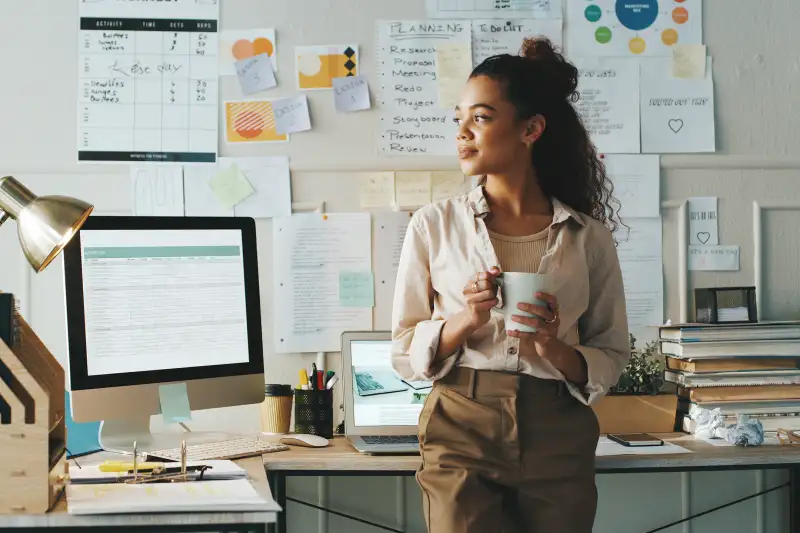 Shot of an attractive young businesswoman standing and looking contemplative while holding a cup of coffee in her home office