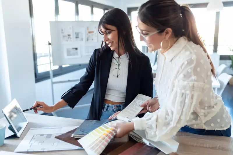 Two beautiful young designer women working in a design project while choosing materials in the office.