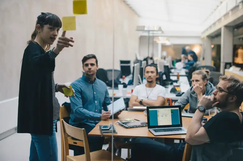 Computer programmer explaining adhesive note while giving presentation to colleagues in office